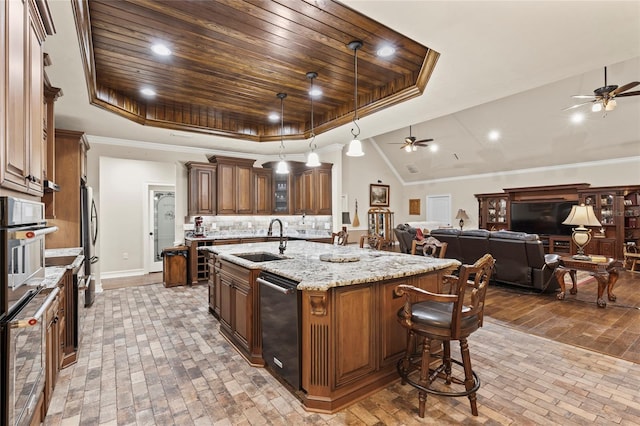 kitchen with an island with sink, a tray ceiling, ceiling fan, and sink