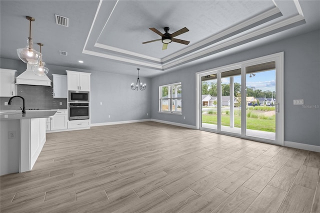 unfurnished living room featuring ceiling fan with notable chandelier, a raised ceiling, and light hardwood / wood-style flooring