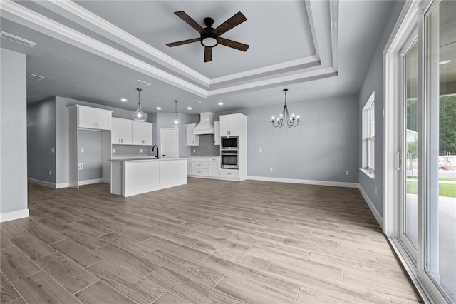 unfurnished living room featuring ceiling fan with notable chandelier, light wood-type flooring, a tray ceiling, and crown molding