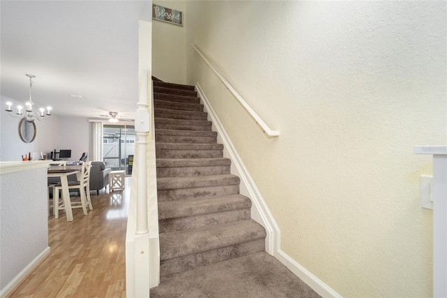 stairway featuring wood-type flooring and ceiling fan with notable chandelier