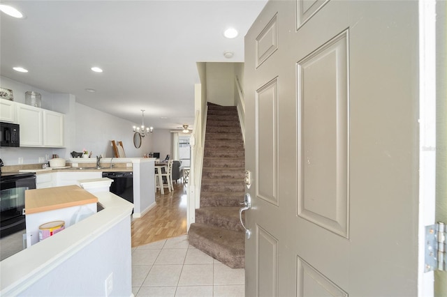 interior space with light countertops, white cabinets, a peninsula, light tile patterned floors, and black appliances