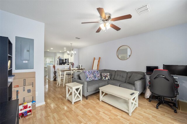 living room with light wood-style flooring, electric panel, ceiling fan with notable chandelier, and visible vents