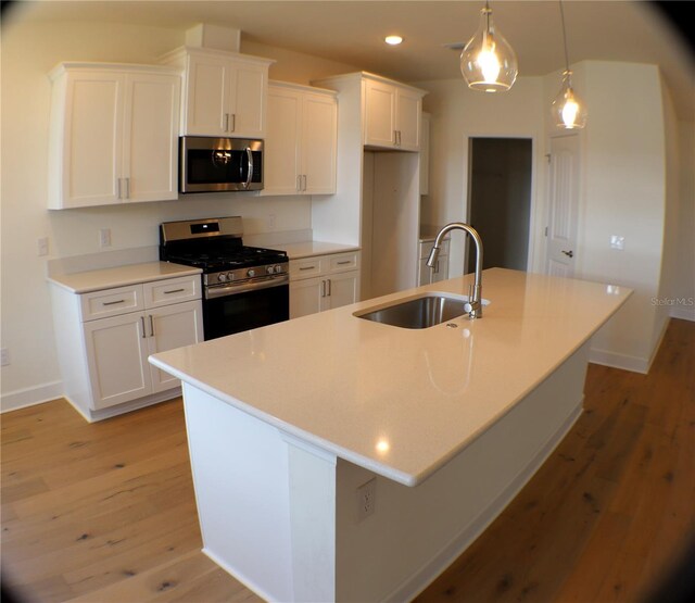 kitchen with stainless steel appliances, a kitchen island with sink, sink, decorative light fixtures, and white cabinets