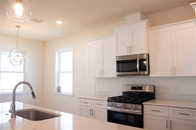 kitchen featuring white cabinets, sink, hanging light fixtures, a notable chandelier, and stainless steel appliances