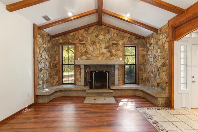 unfurnished living room with a fireplace, lofted ceiling with beams, a wealth of natural light, and hardwood / wood-style floors