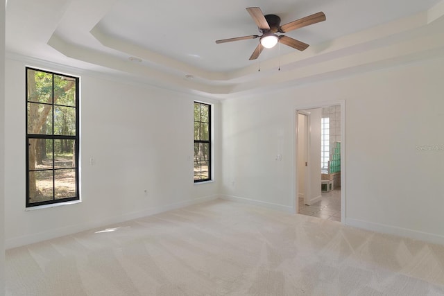 unfurnished room featuring a healthy amount of sunlight, ceiling fan, and a tray ceiling