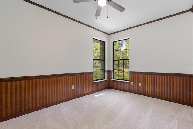 carpeted spare room with wood walls, ceiling fan, and crown molding