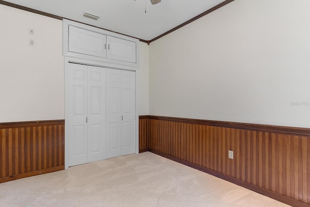 unfurnished bedroom featuring a closet, ornamental molding, carpet flooring, ceiling fan, and wooden walls