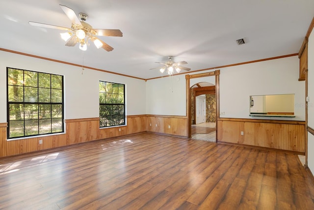 spare room featuring ceiling fan, ornamental molding, hardwood / wood-style floors, and wooden walls