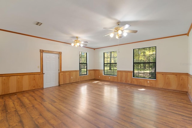 empty room with wood walls, ceiling fan, crown molding, and wood-type flooring