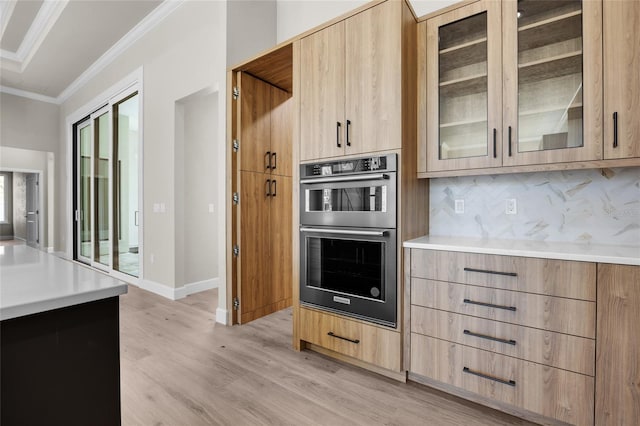 kitchen with light brown cabinets, stainless steel double oven, ornamental molding, backsplash, and light wood-type flooring