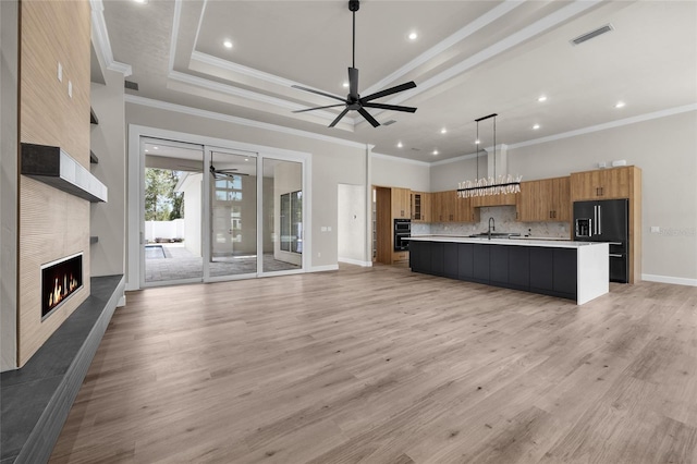 kitchen featuring a tile fireplace, a large island, black fridge, pendant lighting, and light hardwood / wood-style floors