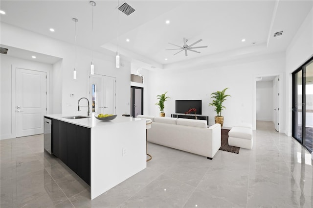 kitchen featuring hanging light fixtures, an island with sink, a tray ceiling, sink, and light tile flooring