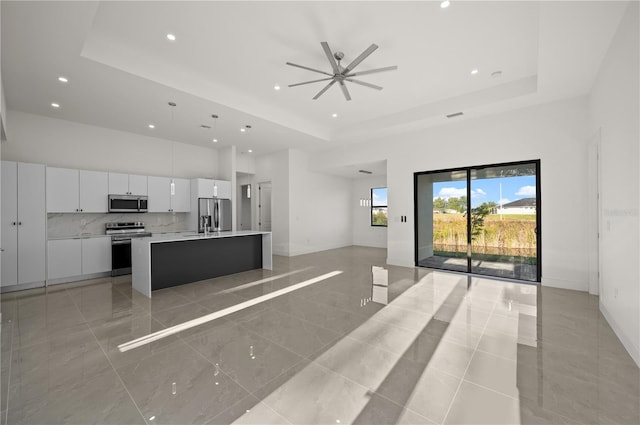 kitchen featuring white cabinetry, a center island with sink, stainless steel appliances, a tray ceiling, and light tile floors