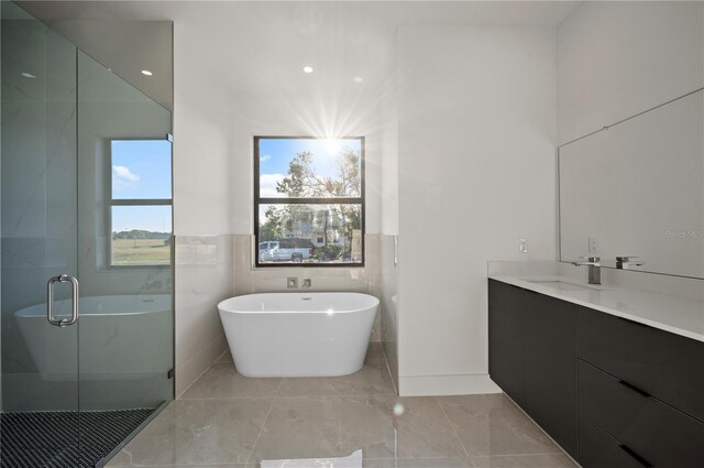 bathroom with tile floors, tile walls, shower with separate bathtub, and vanity