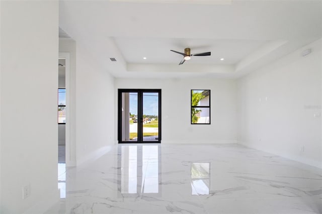 tiled empty room with ceiling fan and a tray ceiling