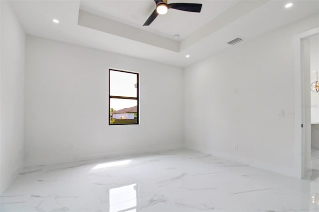 spare room with light tile floors, ceiling fan, and a raised ceiling