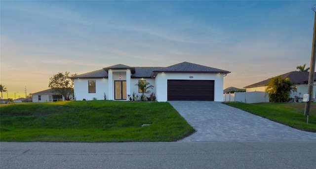 prairie-style house with an attached garage, decorative driveway, a front lawn, and fence