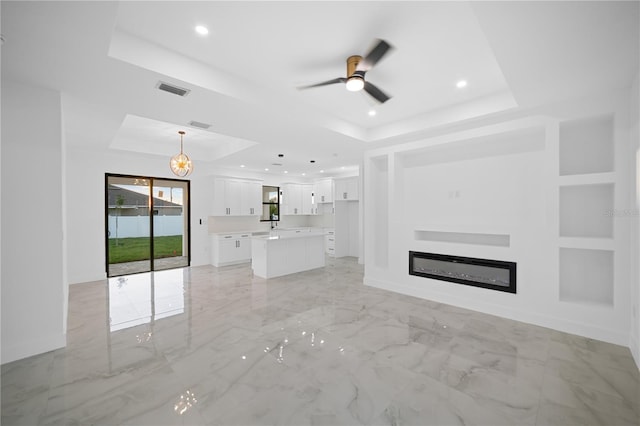 unfurnished living room with visible vents, recessed lighting, a glass covered fireplace, a raised ceiling, and marble finish floor