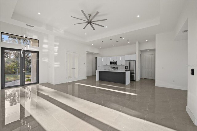 tiled living room featuring ceiling fan, a tray ceiling, and french doors