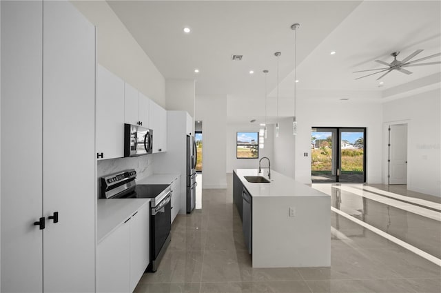 kitchen with light countertops, hanging light fixtures, appliances with stainless steel finishes, white cabinets, and an island with sink