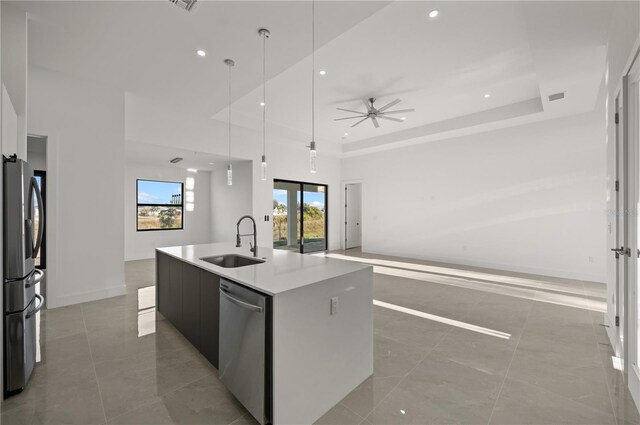 kitchen featuring a tray ceiling, tile floors, an island with sink, appliances with stainless steel finishes, and sink