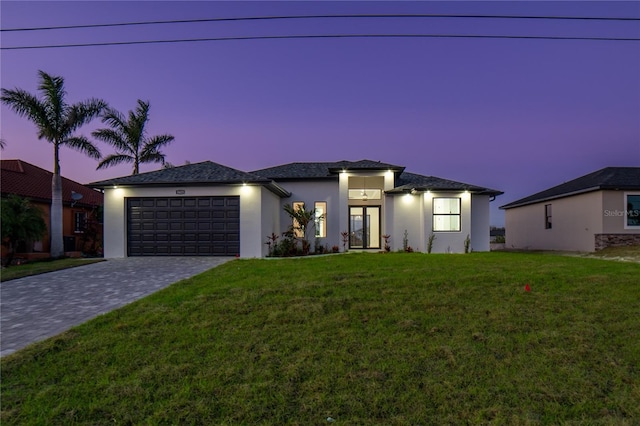 prairie-style home featuring decorative driveway, a lawn, an attached garage, and stucco siding