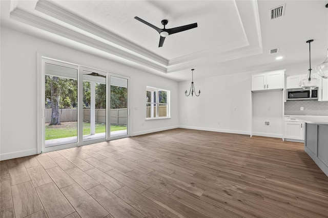 unfurnished living room featuring ceiling fan with notable chandelier, a raised ceiling, hardwood / wood-style flooring, and crown molding