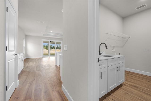 corridor featuring a tray ceiling, sink, and light hardwood / wood-style flooring