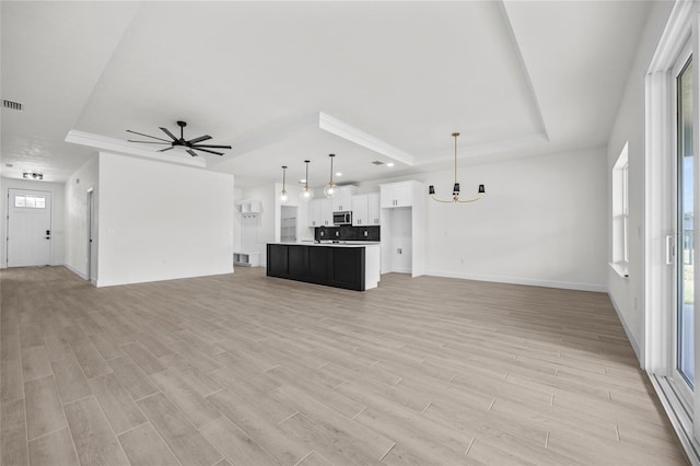 unfurnished living room with ceiling fan with notable chandelier, a raised ceiling, and light wood-type flooring