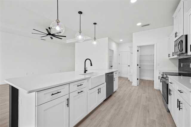 kitchen featuring stainless steel appliances, sink, decorative light fixtures, a center island with sink, and white cabinetry