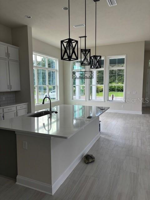 kitchen with sink, a healthy amount of sunlight, an island with sink, and decorative light fixtures