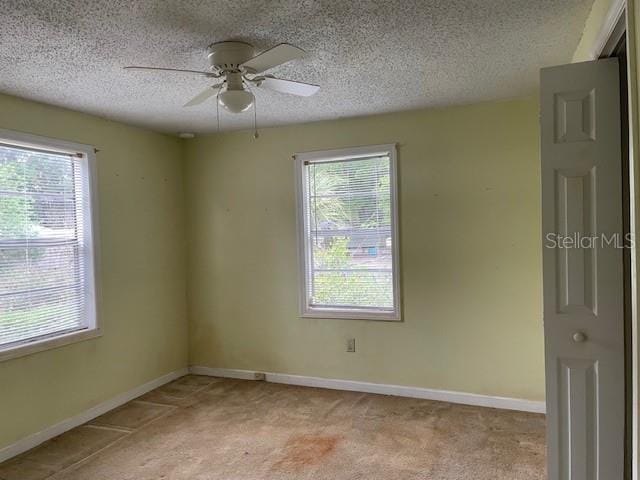 unfurnished room featuring light colored carpet, ceiling fan, a textured ceiling, and a wealth of natural light