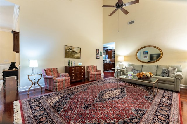 living room with a towering ceiling, dark hardwood / wood-style flooring, ceiling fan, and crown molding