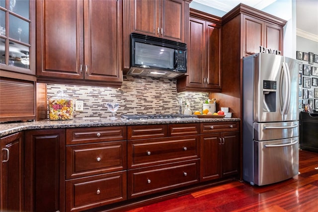 kitchen featuring crown molding, tasteful backsplash, dark stone countertops, dark wood-type flooring, and appliances with stainless steel finishes