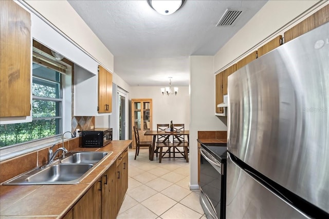 kitchen with sink, light tile floors, hanging light fixtures, stainless steel appliances, and an inviting chandelier