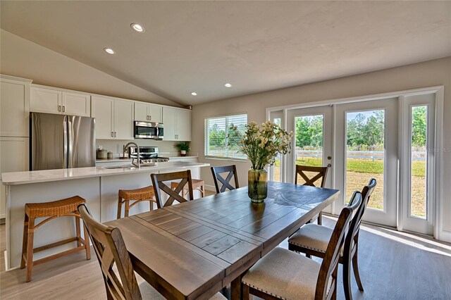 dining space featuring sink, light wood-type flooring, and vaulted ceiling