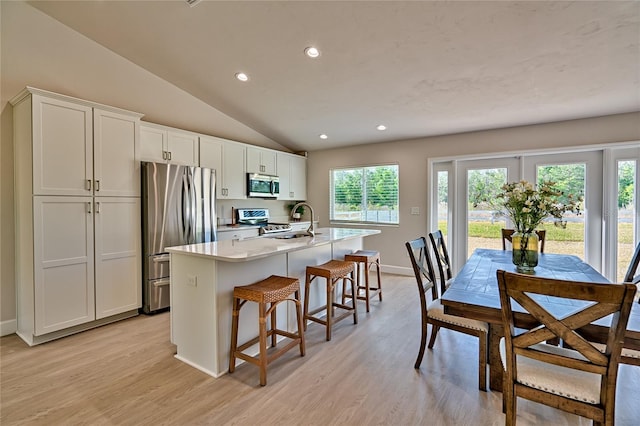 kitchen with a healthy amount of sunlight, appliances with stainless steel finishes, a center island with sink, vaulted ceiling, and light wood-type flooring