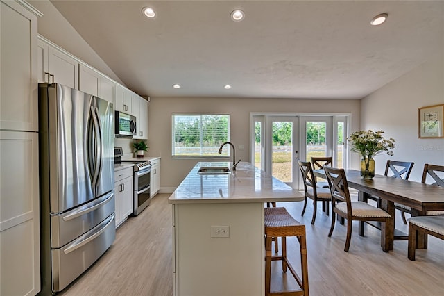 kitchen with appliances with stainless steel finishes, light hardwood / wood-style floors, white cabinetry, a kitchen island with sink, and sink