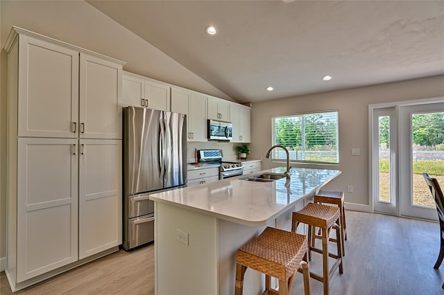 kitchen with white cabinets, sink, light hardwood / wood-style floors, stainless steel appliances, and an island with sink