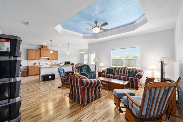 living room with ceiling fan, light wood-type flooring, and a tray ceiling