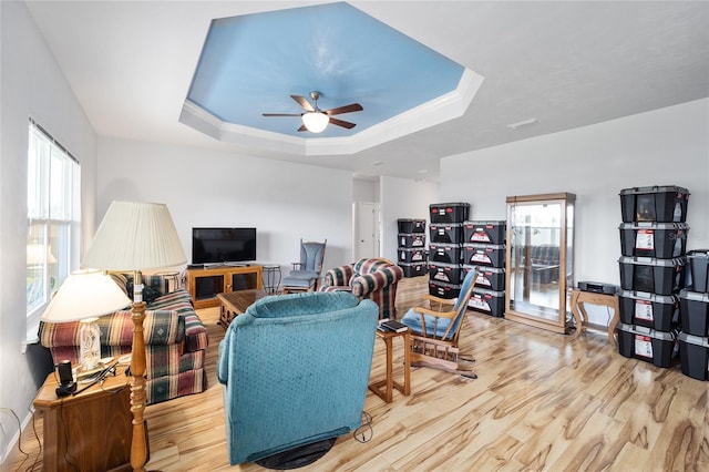 living room featuring ceiling fan, light wood-type flooring, plenty of natural light, and a tray ceiling