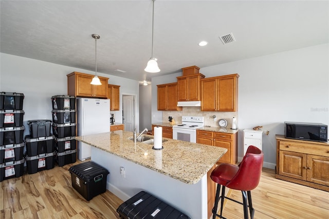 kitchen featuring hanging light fixtures, light wood-type flooring, a breakfast bar area, white appliances, and sink