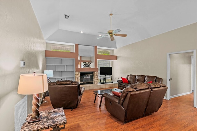 living room featuring ceiling fan, lofted ceiling, light hardwood / wood-style flooring, and a stone fireplace