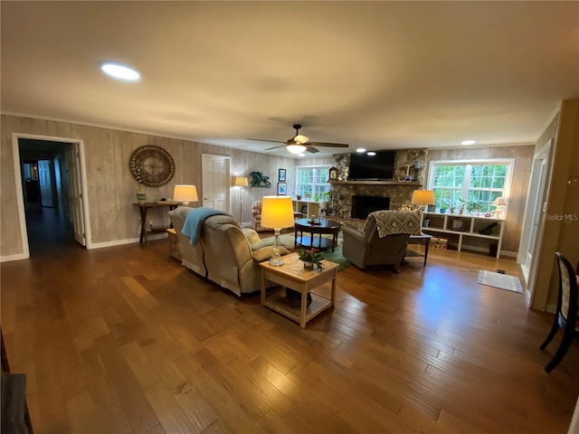 living room featuring wooden walls, ceiling fan, hardwood / wood-style floors, and a stone fireplace