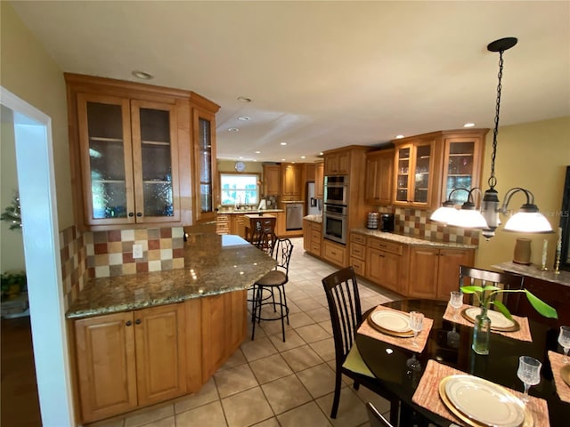 kitchen with tasteful backsplash, pendant lighting, light stone countertops, light tile patterned floors, and double oven