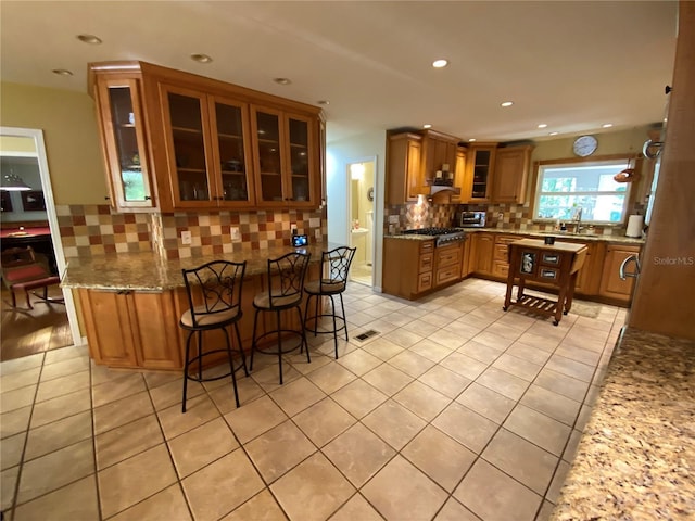 kitchen featuring a kitchen bar, tasteful backsplash, light tile patterned flooring, light stone counters, and sink