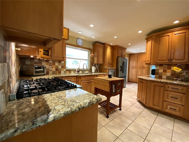 kitchen featuring light stone counters, sink, decorative backsplash, and stainless steel fridge