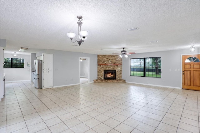 unfurnished living room with light tile patterned floors, ceiling fan with notable chandelier, a brick fireplace, and visible vents