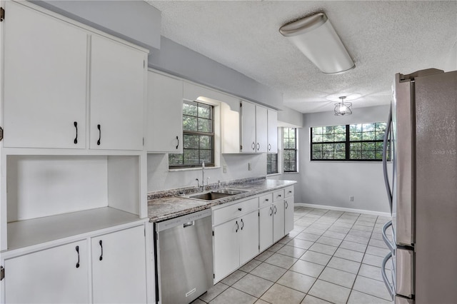 kitchen with appliances with stainless steel finishes, light tile patterned flooring, a sink, and white cabinetry